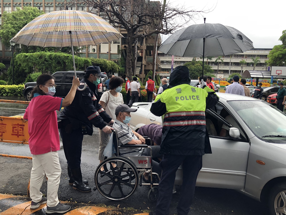 高雄連日大雨，維護秩序的員警們以及工作人員護送長者上車，就像照護自己的家人一樣。(圖片提供/高市府衛生局)