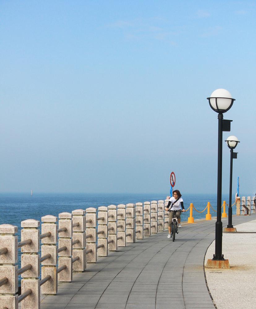 遊客在海岸公園吹海風享受悠閒步調。