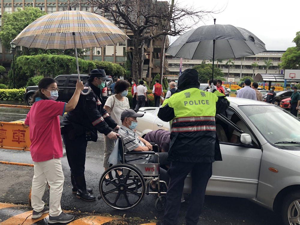高雄連日大雨，維護秩序的員警們以及工作人員護送長者上車，就像照護自己的家人一樣。(圖片提供/高市府衛生局)