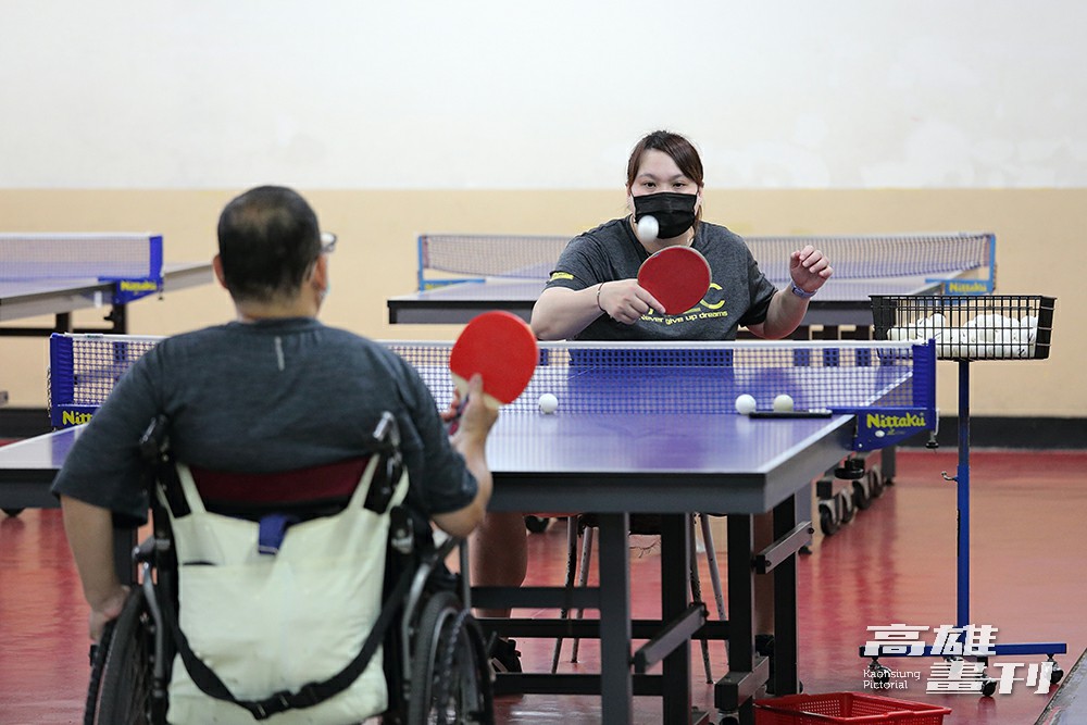 為了與身障者維持同樣高度，蔡貴蘭教練坐在椅子上陪伴肢體障礙者桌球推廣營的學員練球。(攝影/Carter)